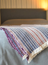 Manta Maison Figo com riscas em tons rosa, azul e bordeaux.